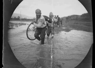 A hired guard helps William Sachtleben carry his bicycle and gear across a stream in Turkey, May 26, 1891, Collection of the UCLA Library Special Collections