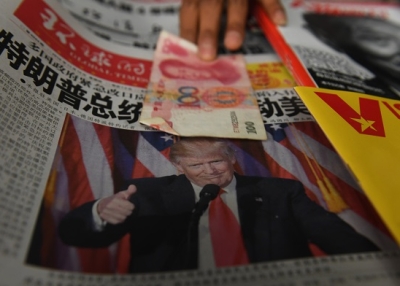 A vendor picks up a 100 yuan note above a newspaper featuring a photo of U.S. President Donald Trump at a news stand in Beijing on November 10, 2016. (Greg Baker/AFP/Getty Images)