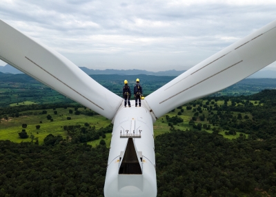 Two Electric engineer wearing Personal protective equipment working on top of wind turbine farm
